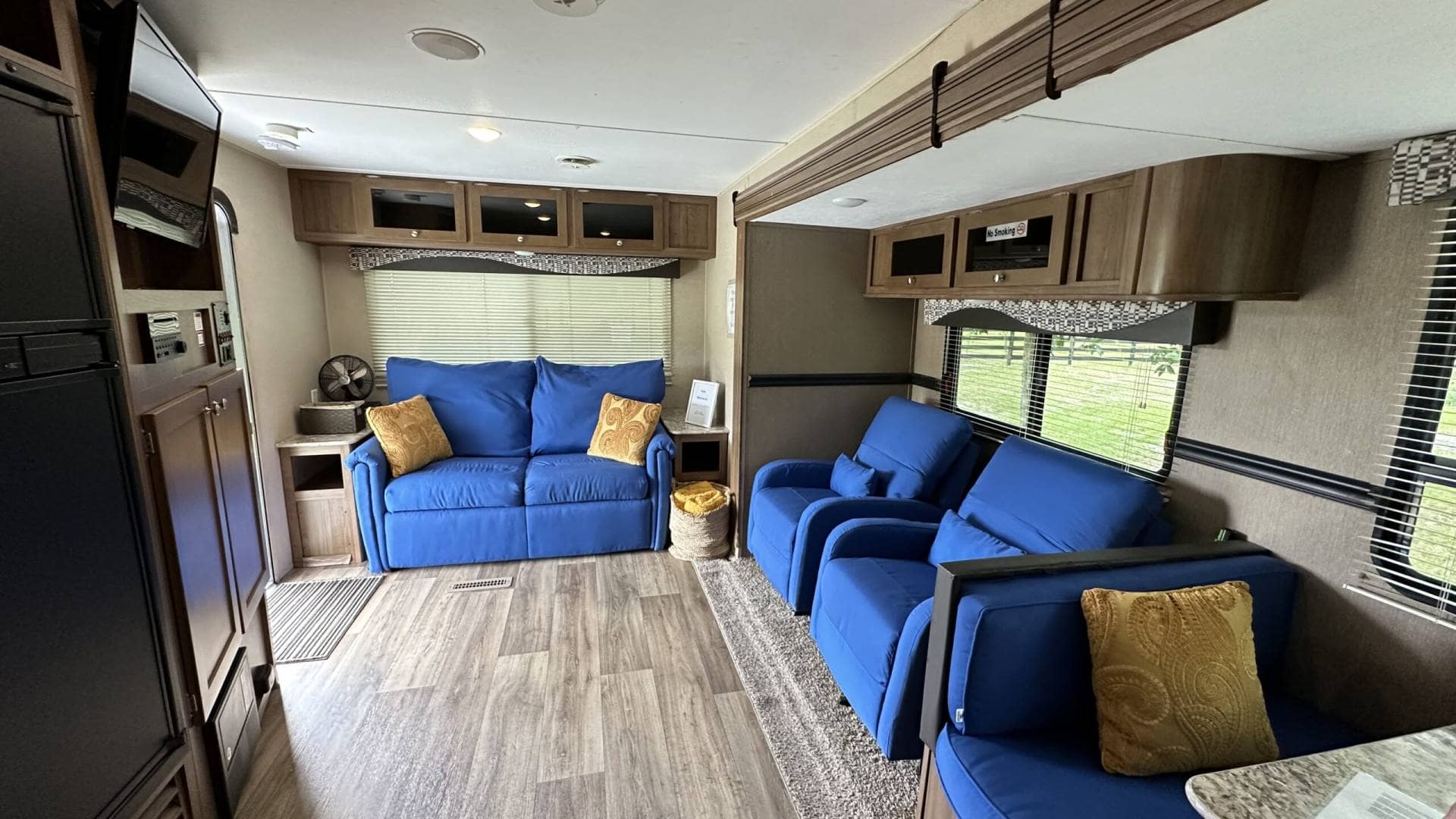 Cozy living room inside a trailer with blue couches and chairs, wooden cabinets, and a window overlooking the countryside at Golden Creek Ranch in Florida.